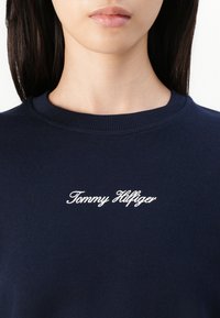 Marineblauwe sweatshirt met een ronde hals en geribde manchetten. Voorzien van witte geborduurde "Tommy Hilfiger" tekst op de borst, met een gladde stofstructuur.