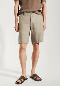 Beige Leinen-Shorts mit Knopfverschluss, flachem Frontdesign und lockerem Sitz, kombiniert mit braunen Riemchensandalen.