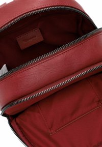 Intérieur d'un sac à dos en cuir rouge, avec une ouverture zippée, une texture lisse et une petite poche intérieure sur le côté.
