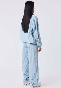 Lichtblauwe windbreaker en broek in een losse pasvorm, gemaakt van glad materiaal. Beschikt over elastische manchetten en bijpassende sneakers met kenmerkende zolen.