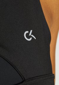 Svart sportkläder med texturerad tyg och en framträdande silverfärgad tillgänglighetssymbol. Designen är snygg och kroppsnära.