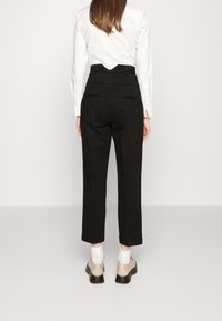 Svarta högmidjade byxor med rak ben, med bakfickor och en slät yta, ihop med beige skor och vita strumpor.