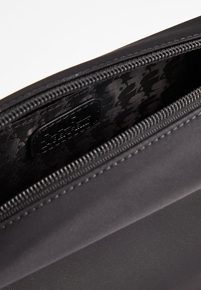 Pochette nera con zip, caratterizzata da un esterno liscio e un rivestimento interno a motivi. Etichetta interna visibile, con tessuto texturizzato attorno alla zip.