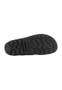Black rubber shoe sole featuring deep tread patterns, ridges, and perforations for traction and flexibility. Durable and textured surface.