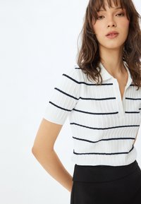 Witte polo shirt met korte mouwen, voorzien van marineblauwe horizontale strepen en een geribbelde textuur. Het heeft een kraag met knopen en een getailleerd ontwerp.