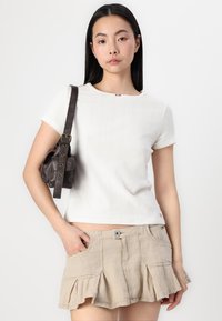 Hvit ribbet kortermet topp med bølgede kanter, sammen med beige volangshorts og en liten brun skinnbag med gulldetaljer.