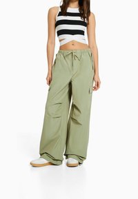 Kvinna i vida olivgröna cargobyxor, vita sneakers och en svartvit randig croppad t-shirt med korskorsdetalj.