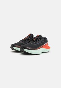 Des chaussures de sport noires avec une tige en maille, rehaussées de rouge et de bleu, dotées d'un épais intercalaire vert menthe et d'une semelle extérieure noire texturée.