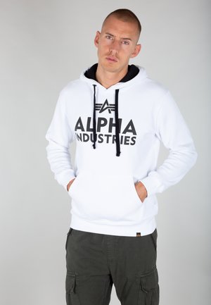 Weißer Kapuzenpullover mit schwarzen Kordeln und "ALPHA INDUSTRIES" in großen schwarzen Buchstaben auf der Vorderseite; mit einer Kängurutasche.