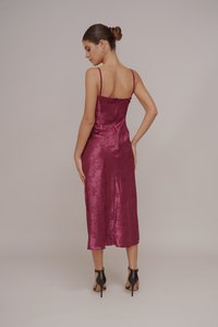 Burgundinės satino midi suknelės su plonomis petnešėlėmis, elegantiška siluetu, gėlių raštas ir žemas nugaros iškirpimas. Dėvima su juodais aukštakulniais bateliais.