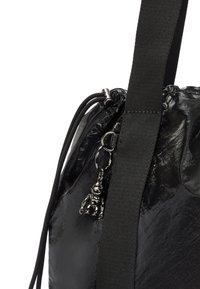 Czarna torba o błyszczącej teksturze, z zamknięciem na sznurek, wytrzymałym paskiem z tkaniny oraz dołączonym srebrnym charms.