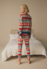 Pajama souprava s červeným a námořnickým vzorem, která obsahuje text "HO", sněhové vločky a stromy; vyrobena z měkké látky, se přiléhavým designem a dlouhým rukávem s elastickými manžetami.