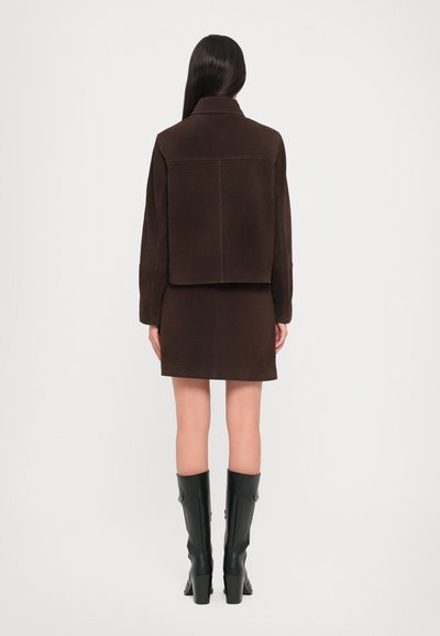 Brown suede jacket with a cropped design and collar, paired with a matching brown mini skirt. Black knee-high heeled boots complete the look.