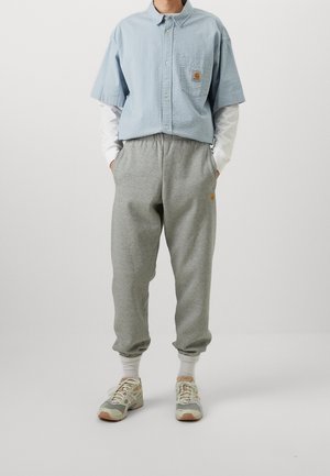 Person wearing light blue short-sleeve shirt layered over white long sleeves, gray sweatpants, white socks, and beige running shoes standing.