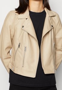 Beige leren bikerjack met een asymmetrische ritsluiting, twee ritssluitingen aan de voorkant en drukknopaccenten op de kraag en manchetten.