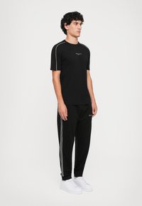 Svart t-skjorte med korte ermer og hvite detaljer, sammen med svarte joggebukser med hvite sidestriper og hvite sneakers.