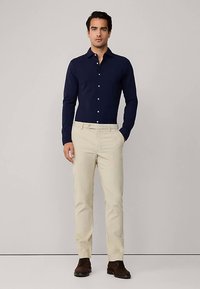 Laivastonsininen pitkähihainen paita napillisella kauluksella, yhdistetty beigenvärisiin housuihin ja tummanruskeisiin kenkiin. Sileä kangas ja istuva malli.