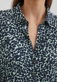 Kragenhemd in Mintgrün mit einem navyblauen abstrakten Muster, ausgestattet mit einer Knopfleiste und einer weichen Stoffstruktur.