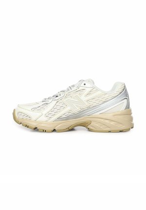 Zapatilla deportiva New Balance en blanco y beige con paneles de malla, suela acolchada y diseño con cordones, mostrada de perfil.