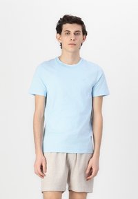 Ανοιχτού μπλε βαμβακερό μπλουζάκι με κοντά μανίκια και στρογγυλή λαιμόκοψη. Διαθέτει ένα διακριτικό λογότυπο στο στήθος και συνδυάζεται με ανοιχτόχρωμο σορτσάκι.