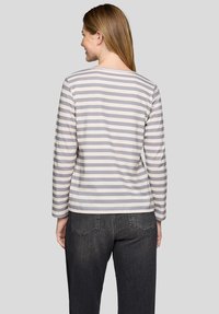 Langärmliges gestreiftes Oberteil aus hellgrauer und beiger Baumwolle mit rundem Ausschnitt und geradem Saum, getragen mit dunklen Denim-Jeans, von hinten betrachtet.