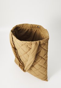 Kváltott táska földszínű barna árnyalatban, amely puha tapintású, tartós anyagból készült, és két hosszú fogantyúval rendelkezik a könnyű hordozhatóság érdekében. Nagy, nyitott tetejű kialakítás.