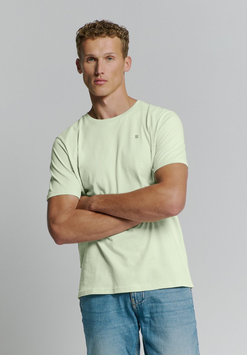 Lichtgroene t-shirt met korte mouwen van zachte katoen, met een ronde halslijn en een subtiele logo op de borst, gedragen met blauwe denim jeans.