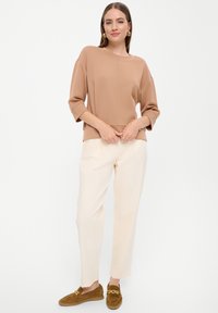 Beige, leichter Pullover mit kastiger Passform und drei Viertelärmeln, kombiniert mit cremefarbenen Hosen. Braune Slipper mit goldenen Hardware-Akzenten.