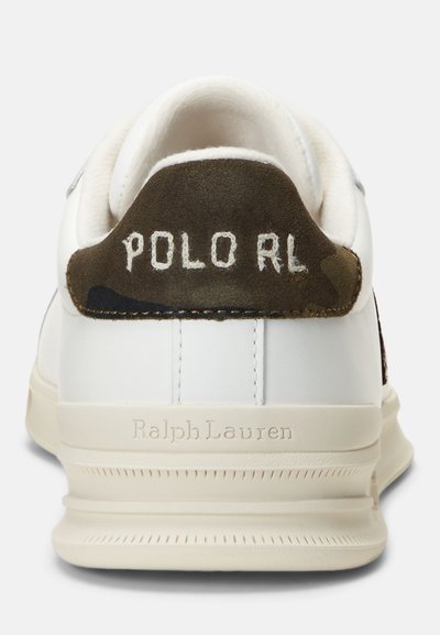 Sneaker bianco in pelle con finitura liscia, caratterizzata da una linguetta sul tallone in suede verde scuro con l'etichetta "POLO RL" cucita in bianco. Dettagli sulla suola testurizzati.