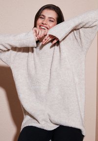 Maglione oversize beige chiaro con polsini a coste, texture morbida e vestibilità rilassata, abbinato a jeans neri scuri.