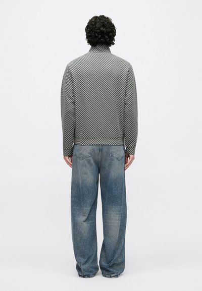 Šedá a biela bunda so vzorom a vysokým golierom, doplnená voľnými modrými rifľami. Jednoduché pozadie.