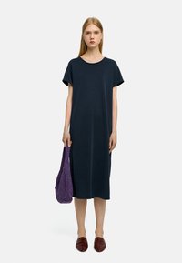 Granatowa bawełniana sukienka midi z krótkimi rękawami, okrągłym dekoltem i luźnym krojem. W towarzystwie plecionej fioletowej torby i brązowych mokasynów.