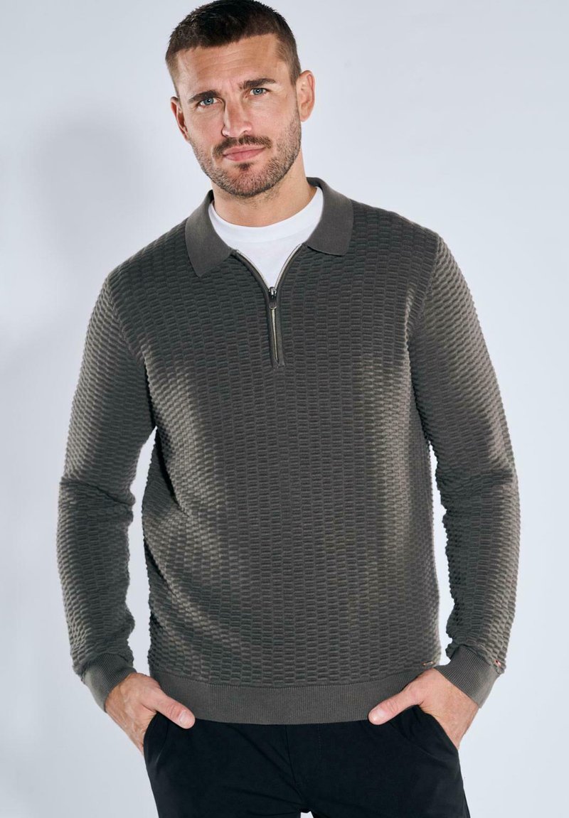 Dunkelgrüner, strukturierter Pullover mit Reißverschlusskragen und kontrastierendem, einfarbigem Kragen. Lange Ärmel mit Gerippteffekten an den Bündchen und dem Saum.