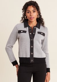 Cardigan tricot noir et blanc avec un motif pied-de-poule, à boutonner sur le devant, col et poignets et ourlet côtelés. Comprend deux poches avant.