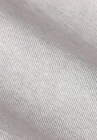 Gros plan sur un tissu gris clair étroitement tissé, avec un motif de sergé diagonal visible et des plis doux.