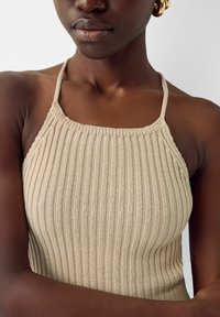 Haut halter en tricot beige côtelé avec des fines bretelles et un décolleté carré, présentant une texture douce et une silhouette ajustée.