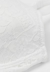 Witte kanten beha met bloemenpatroon, textuur oppervlakte, verstelbare banden en naadloze randen, die fijne details en een zachte uitstraling tentoonstelt.