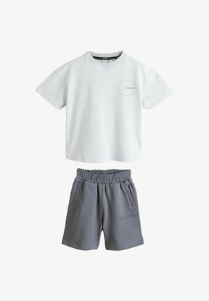 Weißes T-Shirt mit kurzen Ärmeln, rundem Ausschnitt und kleinem Logo, kombiniert mit dunkelgrauen Shorts mit elastischem Bund, Seitentaschen und Logo.