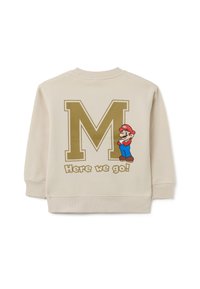 Sudadera crema con una gran "M" dorada y un personaje de dibujos animados con un sombrero rojo y overoles azules, acompañado del texto "¡Aquí vamos!"