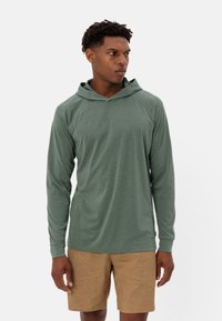 Felpa verde a maniche lunghe con una vestibilità rilassata, caratterizzata da un colletto a V e una texture morbida, abbinata a pantaloncini marrone chiaro.
