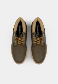 Bocanci din piele maro, cu șiret, având un guler din țesătură bej, talpă ușoară și un logo Timberland proeminent pe interior.
