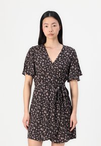 Robe courte noire à fleurs avec des manches courtes, un décolleté en V et une taille à nouer. Elle présente un motif floral à petite échelle en rose et blanc.