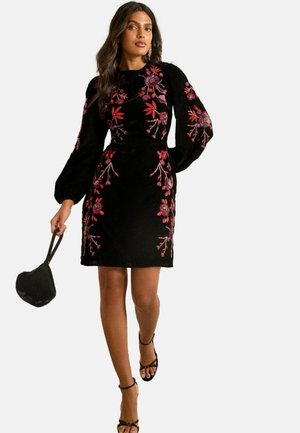 Svart sammetsklänning med långa puffärmar och färgglad blomsterbroderi i rött och lila. Har en figursydd design och knälång längd.