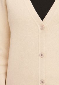 Beige cardigan s výstřihem do V, vyrobený z texturované pleteniny a se třemi knoflíky vpředu. Jednoduchý, klasický styl.