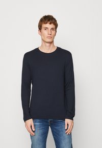 Marineblå langermet T-skjorte laget av myk stoff, med rund hals og enkelt design, kombinert med denim jeans.