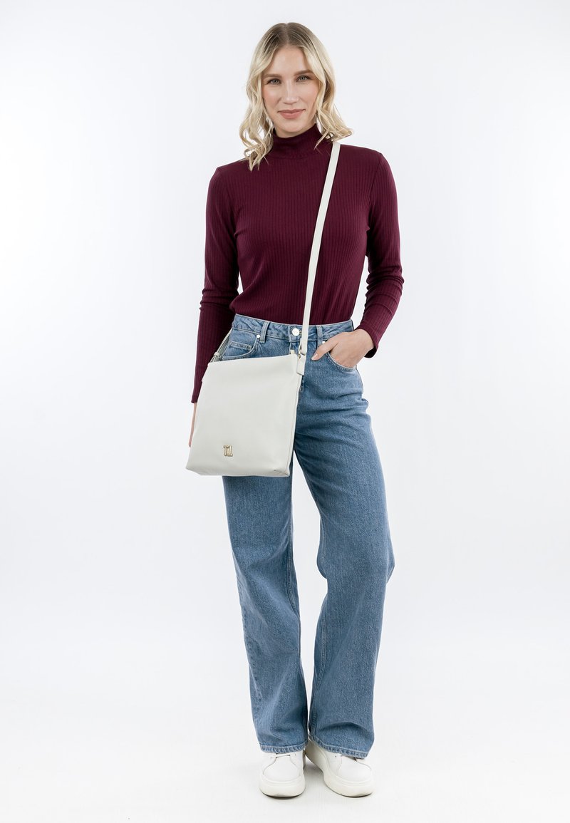Borsa a tracolla bianca con una texture liscia e dettagli in hardware dorato. Modella che indossa un dolcevita bordeaux a coste e jeans blu a vita alta.
