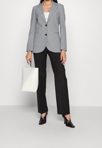 Šedý přizpůsobený blazer s klopami, s dvěma knoflíky, černé kalhoty a bílá strukturovaná kabelka. Podpatky s špičatou špičkou.