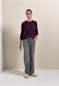 Maglione viola aderente con scollatura rotonda e dettagli sulle cuciture, abbinato a jeans dritti grigi chiari e sneakers bianche.