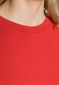 Maglietta in cotone rosso con scollatura rotonda, che mostra una texture liscia e dettagli di cucitura minimi. Il tessuto appare leggero e traspirante.