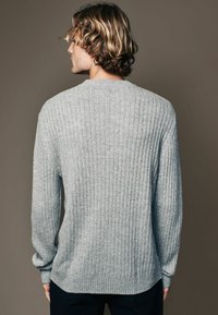 Light gray ribbed knit sweater with a crew neckline and long sleeves, featuring a relaxed fit and a rounded hem at the bottom.